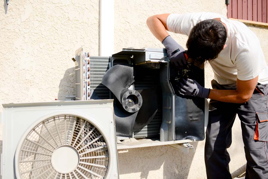 young man electrician installer working on outdoor compressor unit air conditioner at a client's home in hepburn