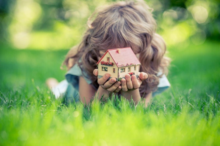 Girl in grass holding little home.