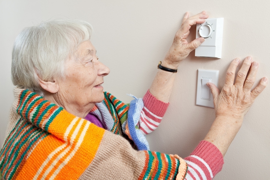 Senior woman ttrying to stay warm by wearing a blanket and adjusting her thermostat. How do I know when it's time for a new furnace.