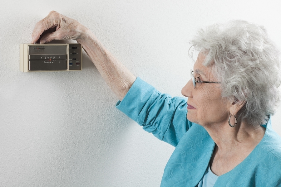 Senior woman adjusting home thermostat. What you need to know for an HVAC emergency.